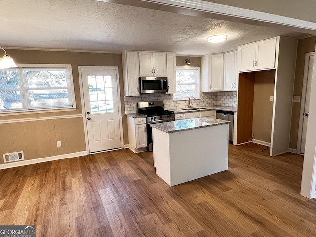 kitchen with a center island, sink, stainless steel appliances, light stone counters, and white cabinets