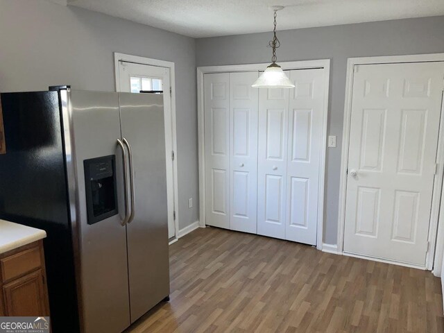 kitchen featuring light wood-type flooring, stainless steel fridge, a textured ceiling, and decorative light fixtures