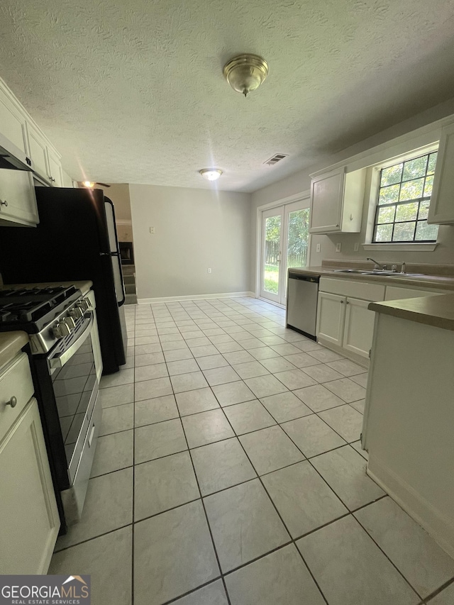 kitchen featuring sink, light tile patterned floors, a textured ceiling, white cabinetry, and stainless steel appliances