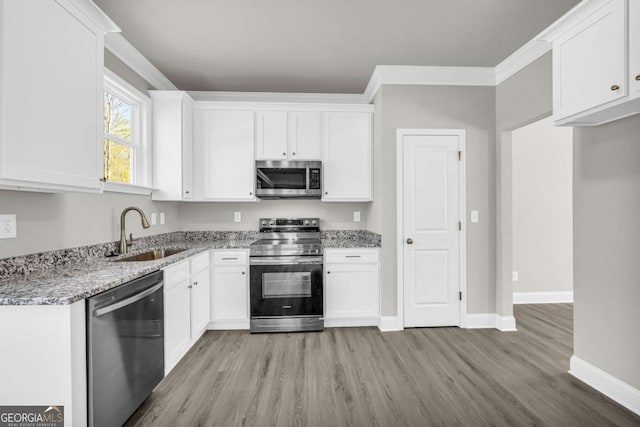 kitchen featuring appliances with stainless steel finishes, light wood-type flooring, light stone counters, sink, and white cabinets