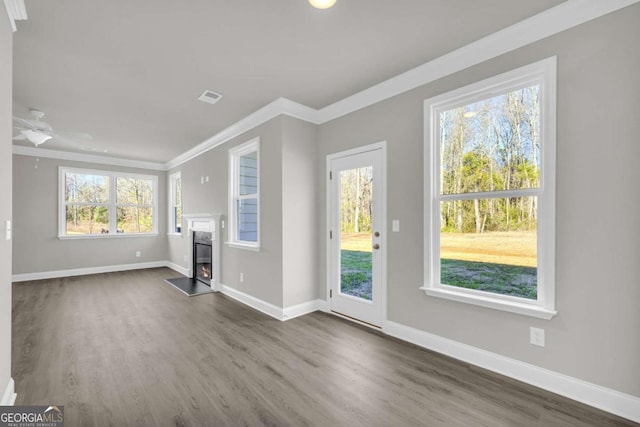 unfurnished living room featuring dark wood-type flooring, a premium fireplace, crown molding, and a healthy amount of sunlight