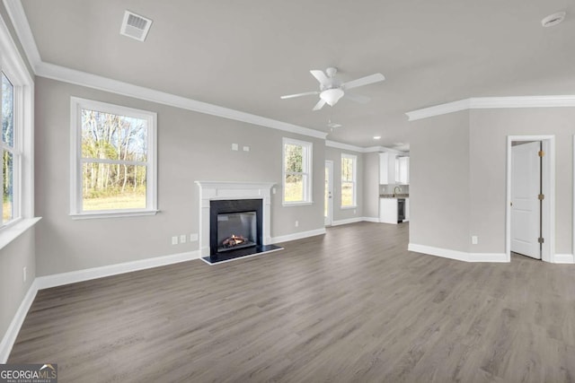 unfurnished living room featuring crown molding, hardwood / wood-style flooring, ceiling fan, a fireplace, and a wealth of natural light