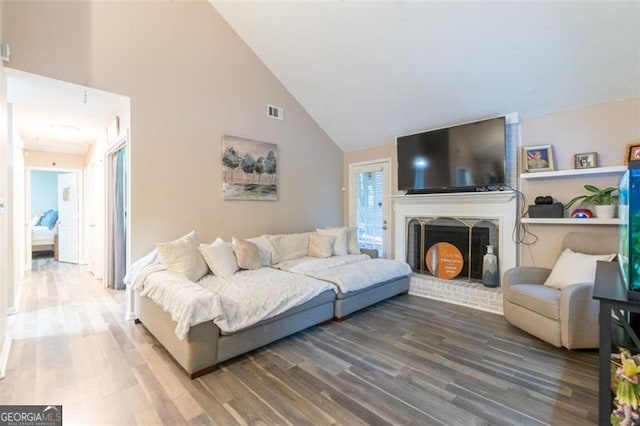 living room with a fireplace, wood-type flooring, high vaulted ceiling, and a healthy amount of sunlight