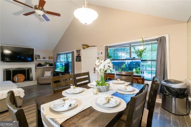 dining area with ceiling fan, a fireplace, high vaulted ceiling, and dark wood-type flooring