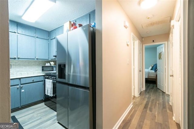 kitchen featuring decorative backsplash, light hardwood / wood-style floors, a textured ceiling, and appliances with stainless steel finishes