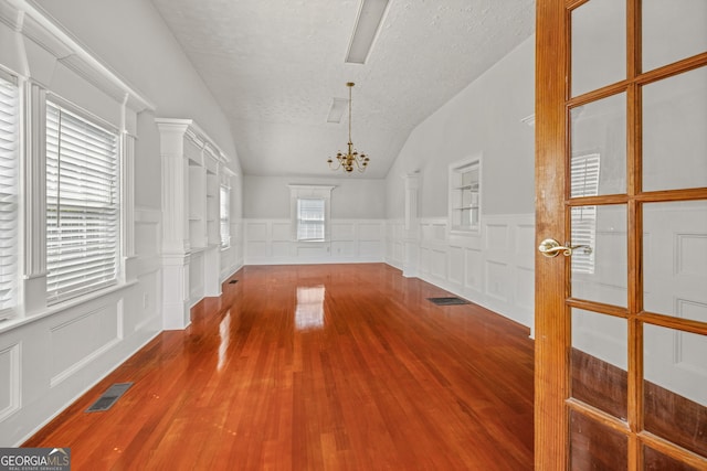 empty room featuring a chandelier, wood-type flooring, a textured ceiling, and lofted ceiling