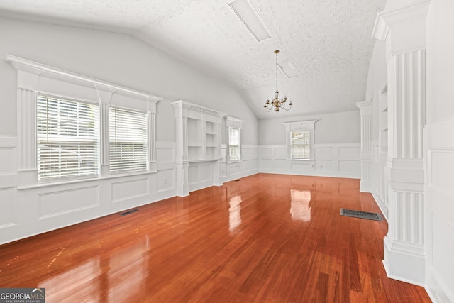 unfurnished living room featuring lofted ceiling, hardwood / wood-style floors, a chandelier, and a textured ceiling