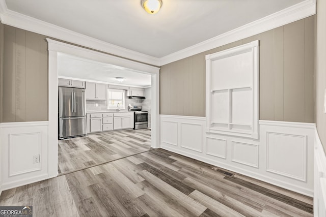 unfurnished living room featuring light wood-type flooring, crown molding, and sink