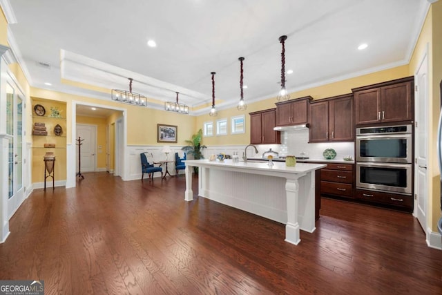 kitchen featuring a center island with sink, a kitchen breakfast bar, hanging light fixtures, dark hardwood / wood-style floors, and stainless steel double oven