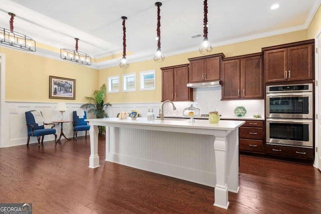 kitchen with a breakfast bar, decorative light fixtures, a center island with sink, and double oven