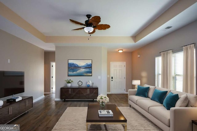 living room featuring dark hardwood / wood-style floors, ceiling fan, and a tray ceiling