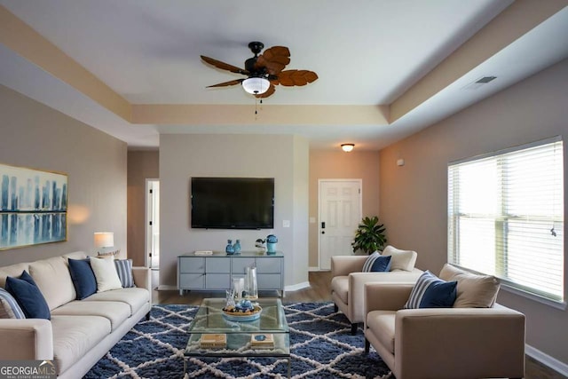 living room with ceiling fan, a raised ceiling, and dark wood-type flooring