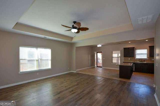 unfurnished living room with dark hardwood / wood-style floors, ceiling fan, a raised ceiling, and sink