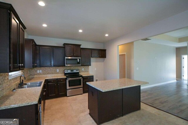 kitchen featuring light stone countertops, appliances with stainless steel finishes, tasteful backsplash, sink, and a center island