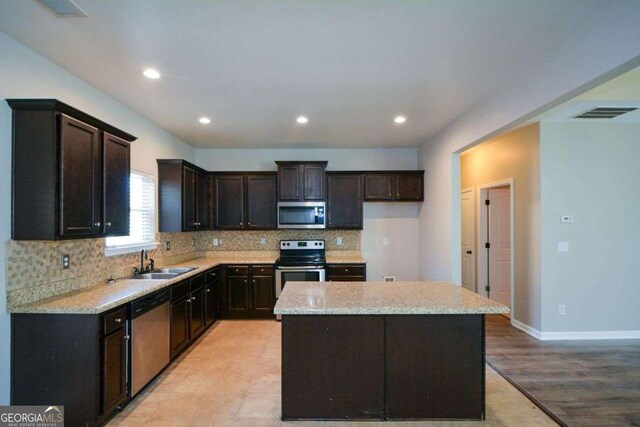 kitchen featuring a center island, backsplash, sink, light stone countertops, and appliances with stainless steel finishes