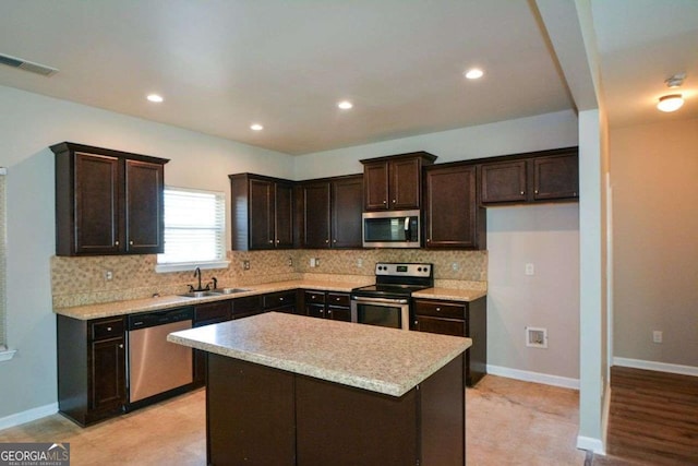 kitchen with light stone countertops, tasteful backsplash, stainless steel appliances, sink, and a center island