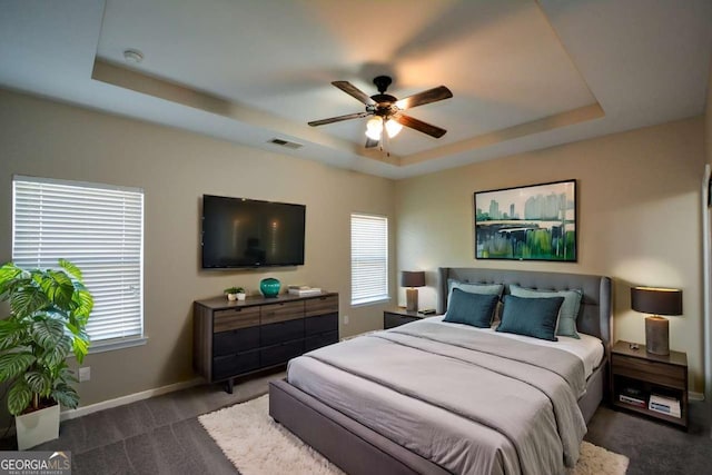 carpeted bedroom featuring multiple windows, a raised ceiling, and ceiling fan