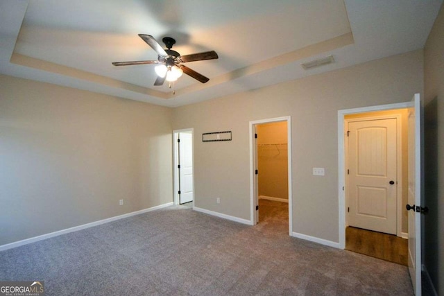 unfurnished bedroom featuring a walk in closet, ceiling fan, a tray ceiling, carpet floors, and a closet