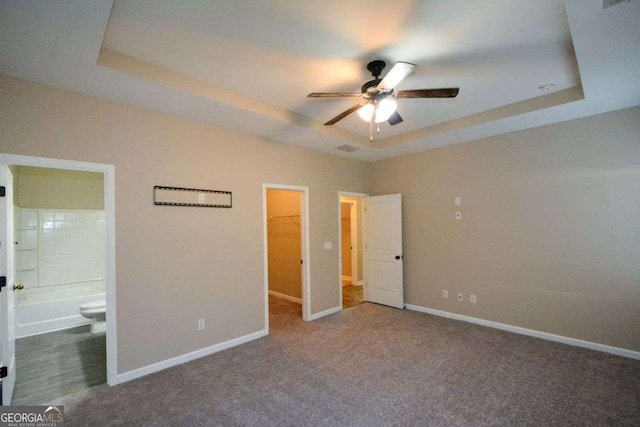 unfurnished bedroom featuring a raised ceiling, ensuite bath, a walk in closet, and a closet