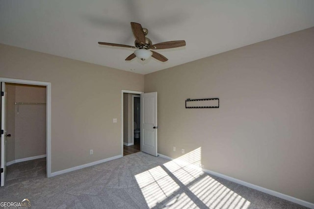 unfurnished bedroom featuring a spacious closet, a closet, ceiling fan, and light colored carpet