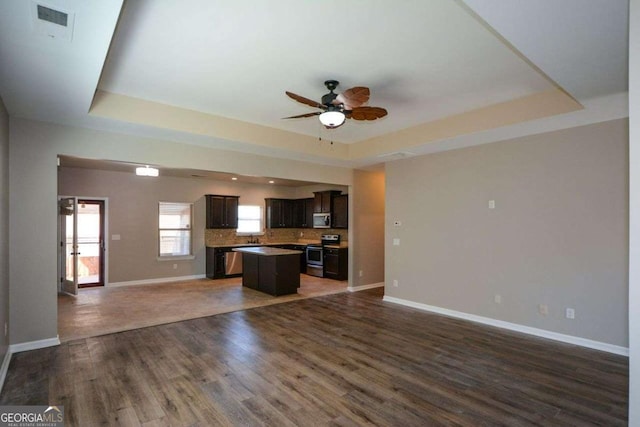 kitchen with a raised ceiling, dark wood-type flooring, a center island, and stainless steel appliances