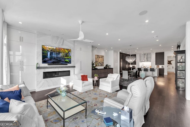 living room with a high end fireplace, ceiling fan with notable chandelier, and hardwood / wood-style flooring