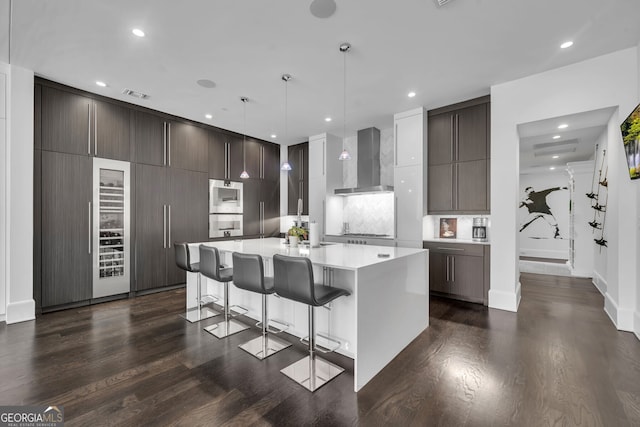 kitchen with a center island, wall chimney exhaust hood, hanging light fixtures, stainless steel gas cooktop, and a breakfast bar