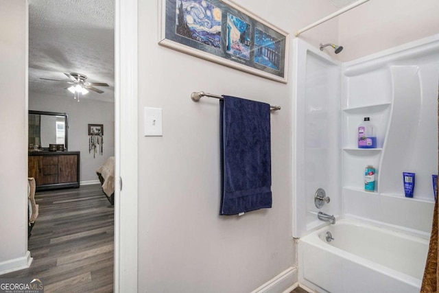 bathroom with ceiling fan, wood-type flooring, washtub / shower combination, and a textured ceiling