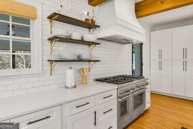 kitchen with light stone counters, premium range hood, range with two ovens, decorative backsplash, and white cabinets