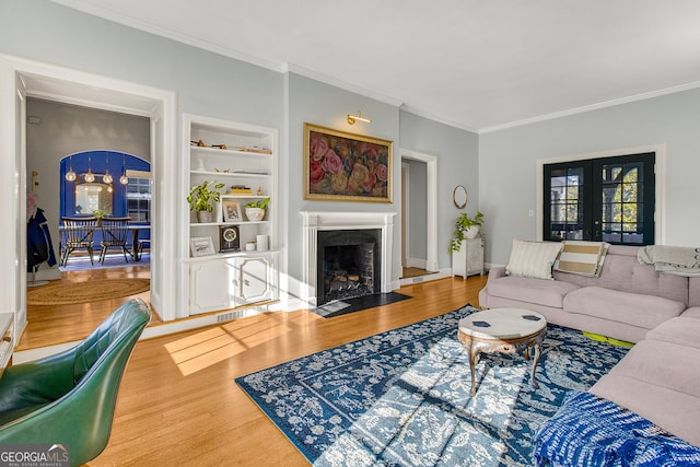 living room with built in shelves, french doors, crown molding, and hardwood / wood-style floors