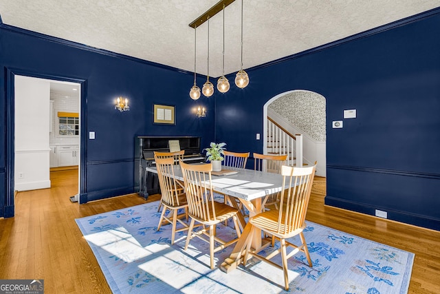 dining space with crown molding, light wood-type flooring, and a textured ceiling