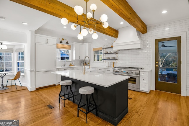 kitchen featuring white cabinets, custom exhaust hood, range with two ovens, and beamed ceiling