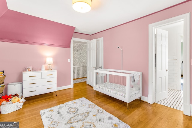 bedroom featuring a crib, light hardwood / wood-style floors, and crown molding