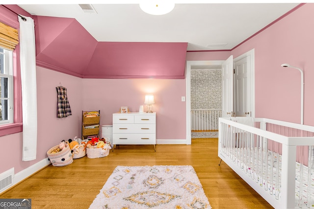 bedroom featuring ornamental molding, lofted ceiling, light hardwood / wood-style flooring, and a nursery area