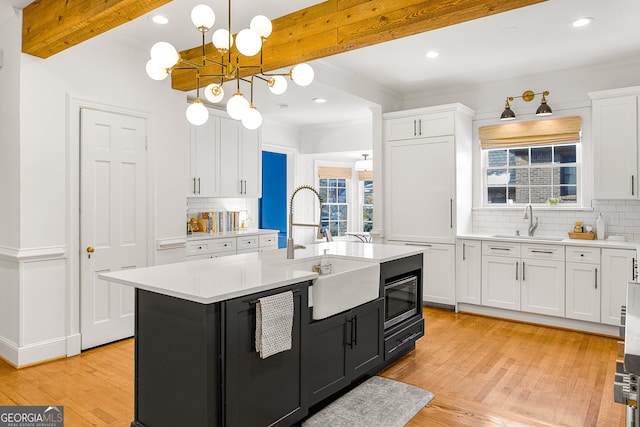 kitchen featuring beamed ceiling, sink, white cabinetry, and an island with sink