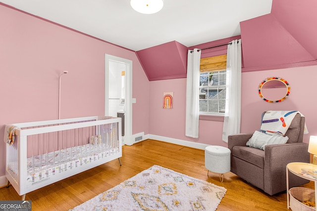 bedroom featuring vaulted ceiling, hardwood / wood-style floors, and a crib