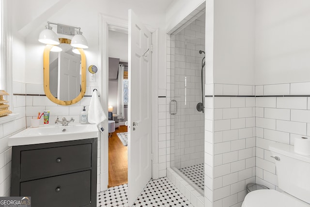 bathroom featuring a shower with door, vanity, tile walls, and toilet