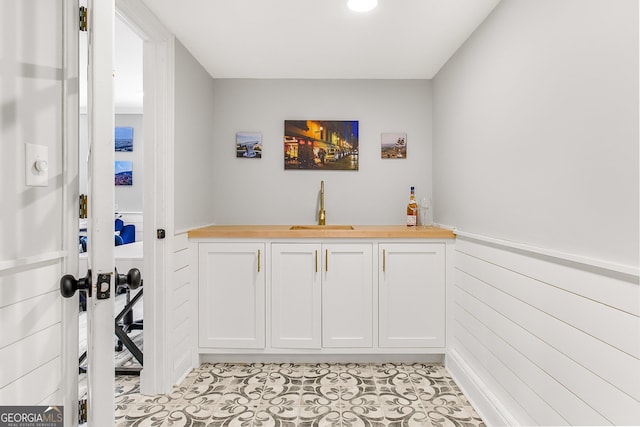 bar with wood counters, light tile patterned floors, white cabinets, and sink