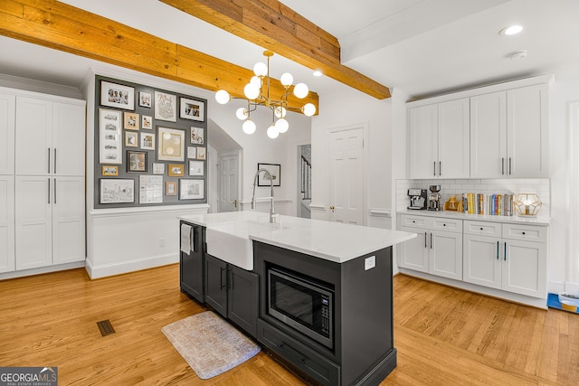 kitchen featuring stainless steel microwave, white cabinets, sink, hanging light fixtures, and beamed ceiling