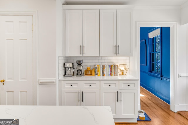 interior space with white cabinetry, decorative backsplash, light stone counters, and light hardwood / wood-style floors