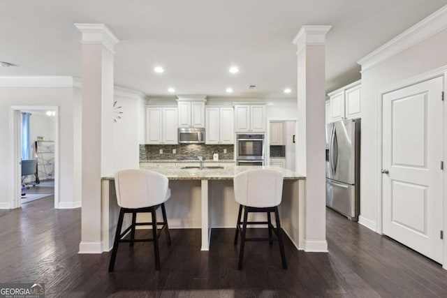 kitchen featuring light stone counters, white cabinetry, stainless steel appliances, and a breakfast bar area