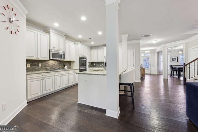 kitchen with light stone counters, stainless steel appliances, dark wood-type flooring, crown molding, and white cabinets