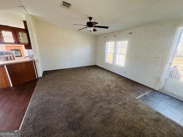 unfurnished living room featuring ceiling fan, dark carpet, and a textured ceiling