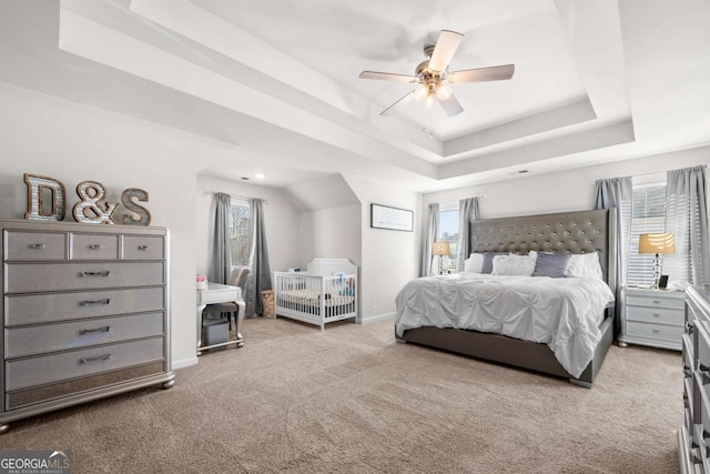 carpeted bedroom featuring ceiling fan, multiple windows, and a tray ceiling