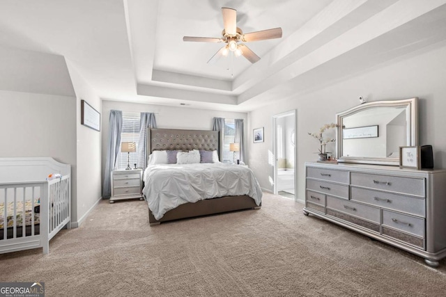 carpeted bedroom with ceiling fan, ensuite bath, and a tray ceiling