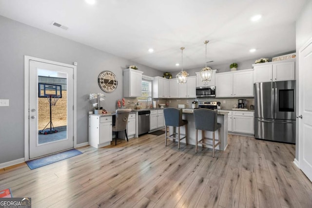 kitchen featuring backsplash, white cabinets, hanging light fixtures, a kitchen island, and stainless steel appliances