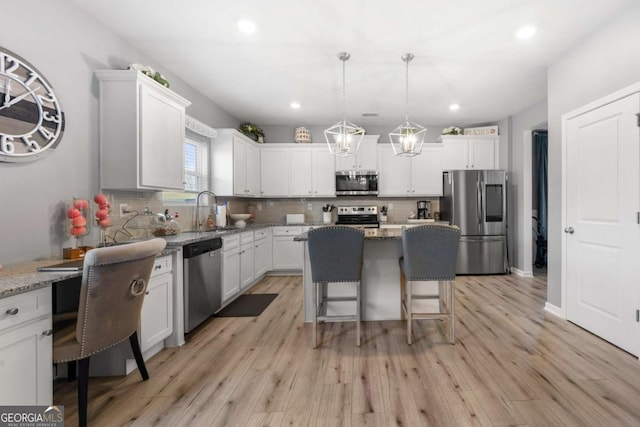 kitchen with white cabinetry, stone counters, a breakfast bar, a kitchen island, and appliances with stainless steel finishes