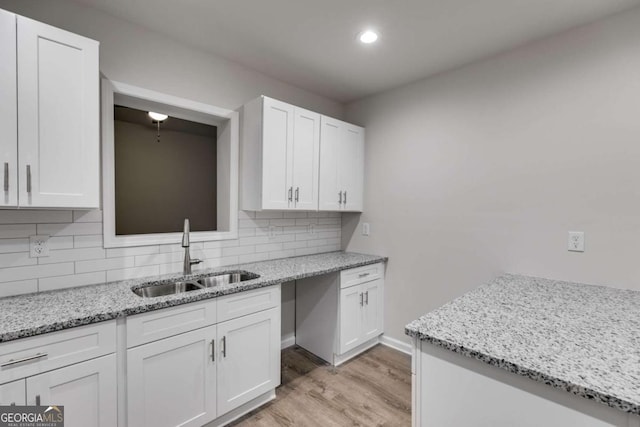 kitchen featuring light stone countertops, sink, decorative backsplash, white cabinets, and light wood-type flooring