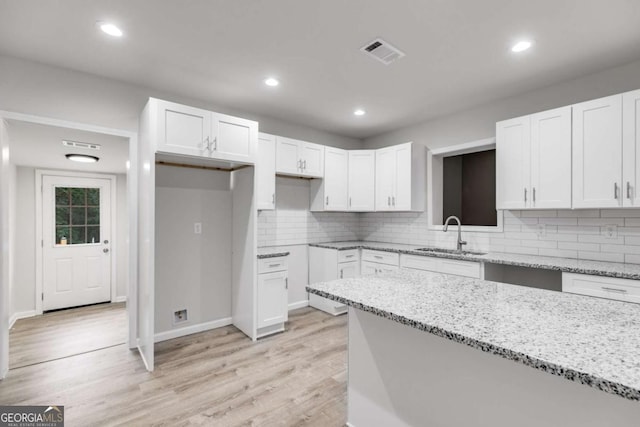 kitchen featuring light stone countertops, tasteful backsplash, sink, light hardwood / wood-style floors, and white cabinetry