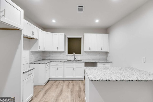 kitchen featuring white cabinets, tasteful backsplash, light stone countertops, and sink